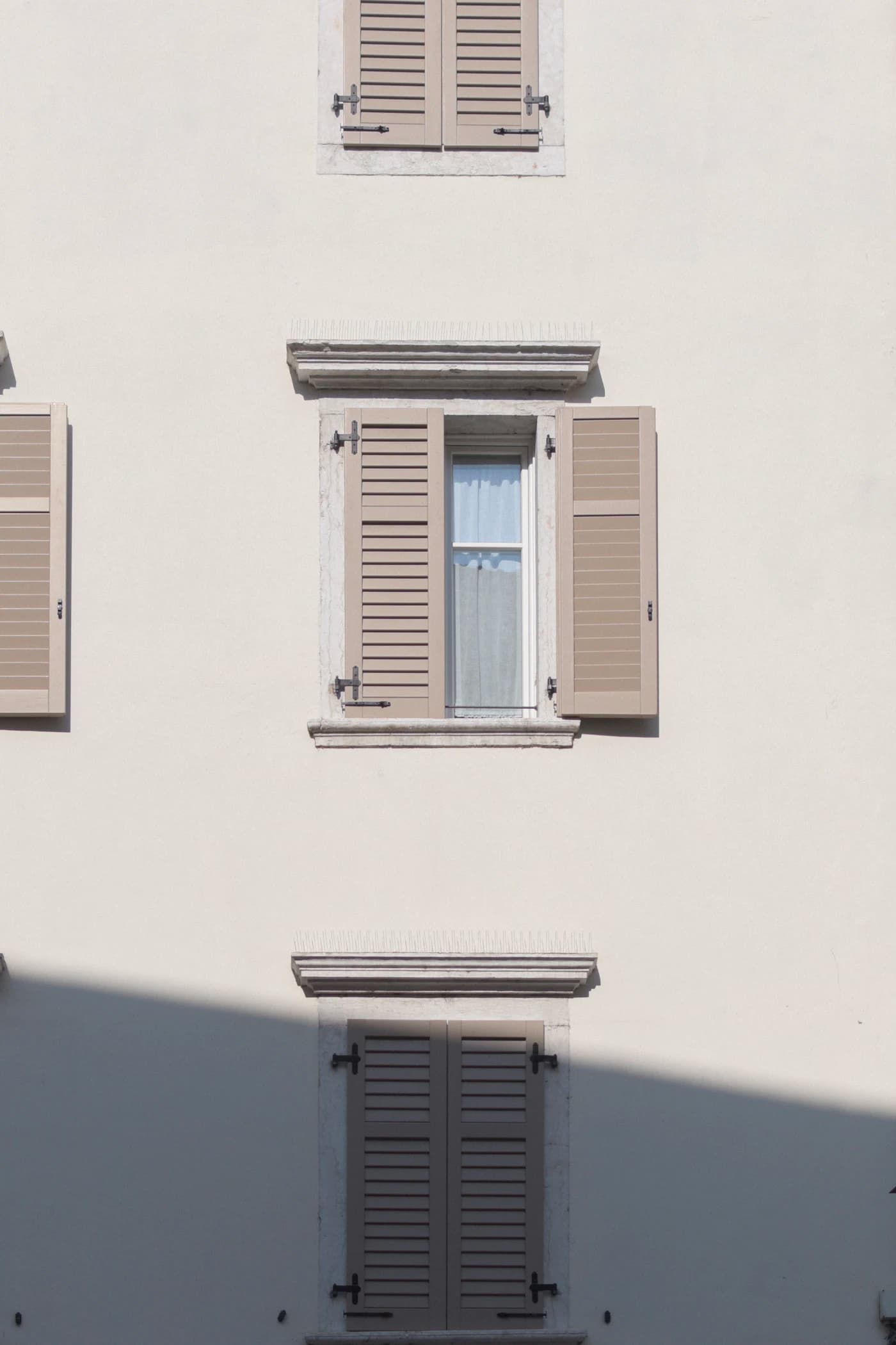 Tan louvered shutters on a cream stucco wall, showing hinges and slats