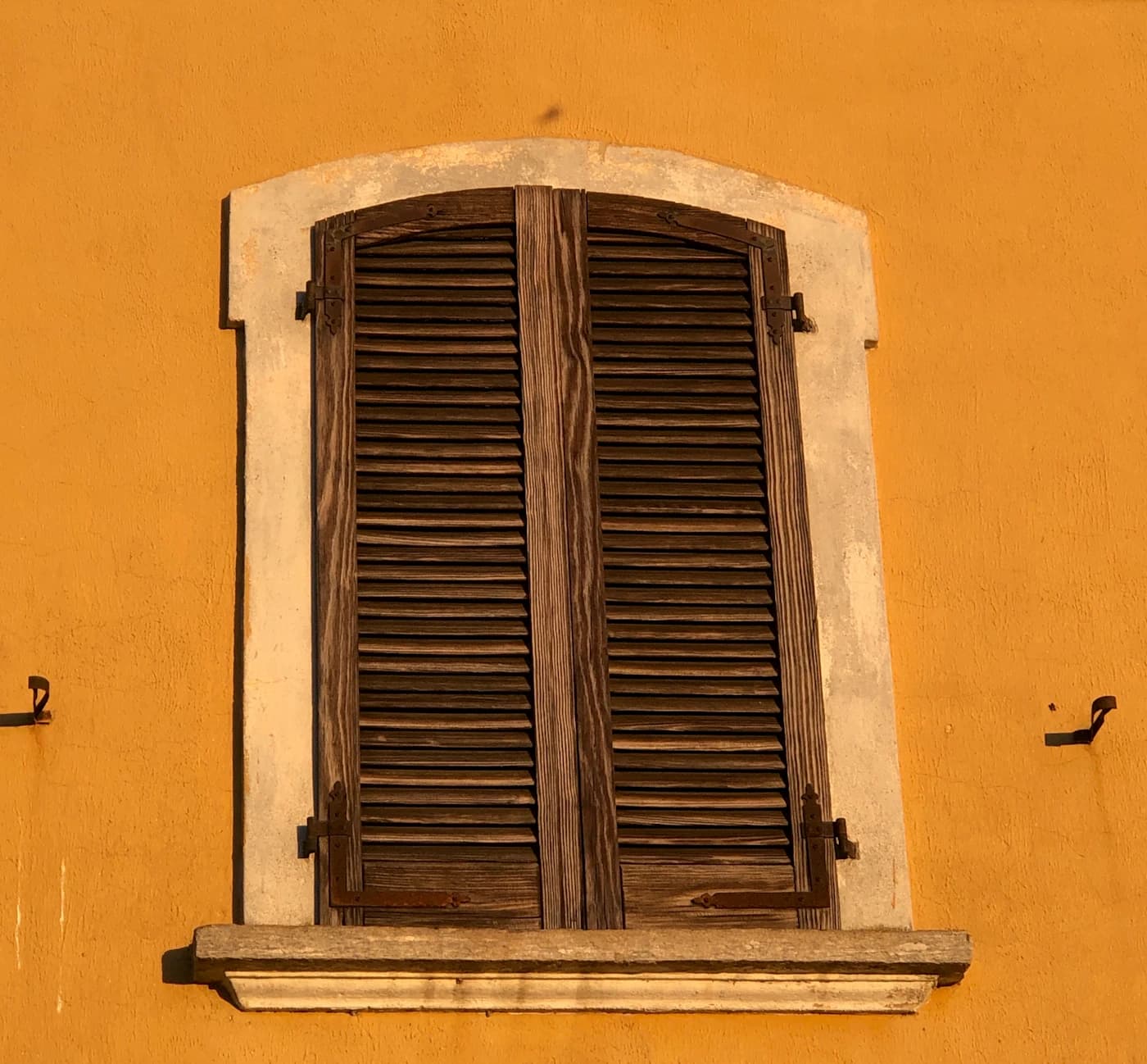 Weathered wooden louvered shutters and metal hinges in sunlight