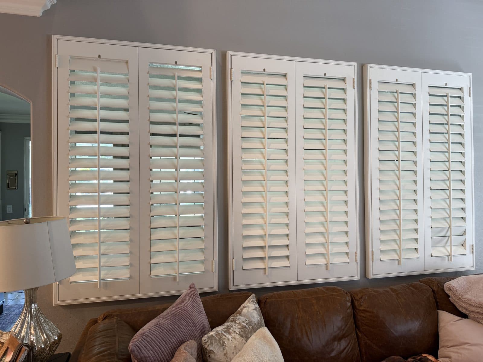Open white plantation shutters on a bedroom window beside a lamp. Real AAA Shutter Repair job photo.