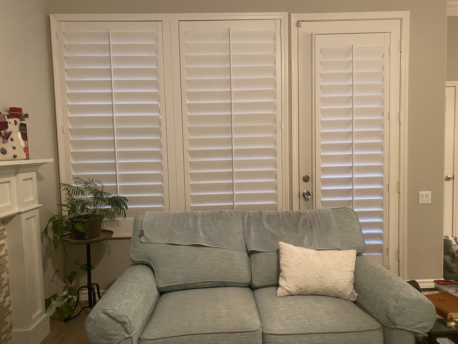 Wide bank of white plantation shutters across a living room window. Real AAA Shutter Repair job photo.
